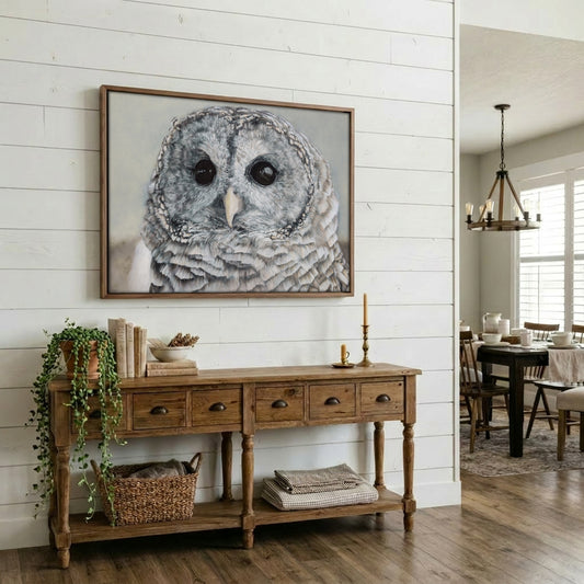 A framed barred owl portrait print hanging on a white shiplap wall above a rustic wooden console table in a bright dining room.