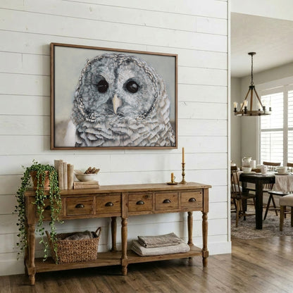 A framed barred owl portrait print hanging on a white shiplap wall above a rustic wooden console table in a bright dining room.