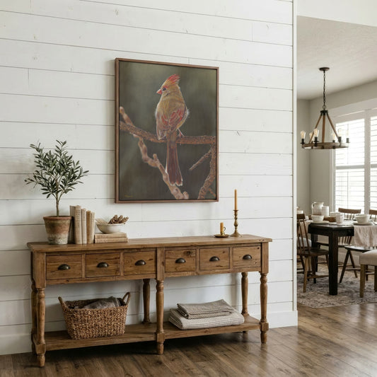 A framed vertical painting of a cardinal on a branch, displayed on a white shiplap wall above a rustic wooden console table in a bright, modern dining room.