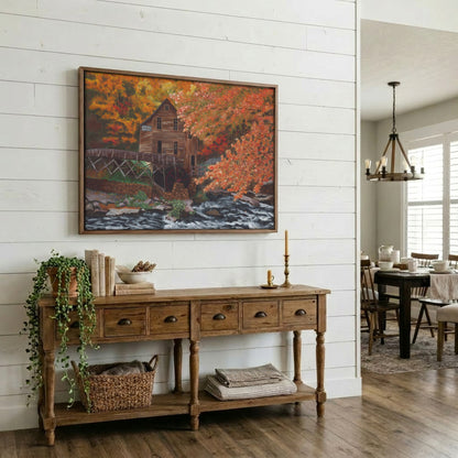 A framed landscape painting of a rustic mill by an autumn river hangs on a white shiplap wall above a wooden console table in a bright, modern farmhouse-style room.