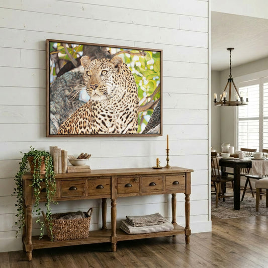 A framed wall art print of a leopard in a tree branch hangs above a rustic wooden console table in a bright, modern dining room with white shiplap walls and hardwood floors.