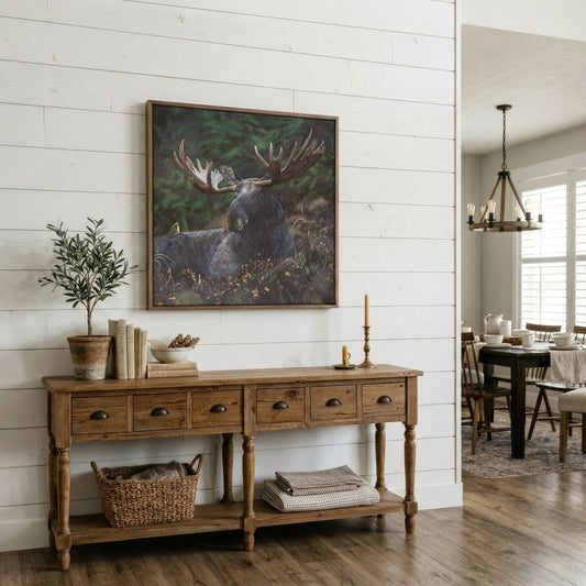 A framed moose painting hangs on a white shiplap wall above a rustic wooden console table in a bright, modern dining room.