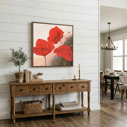 A framed wall art print featuring large red poppies on a soft cream background, displayed above a rustic wooden console table in a bright, white-shiplap dining room.