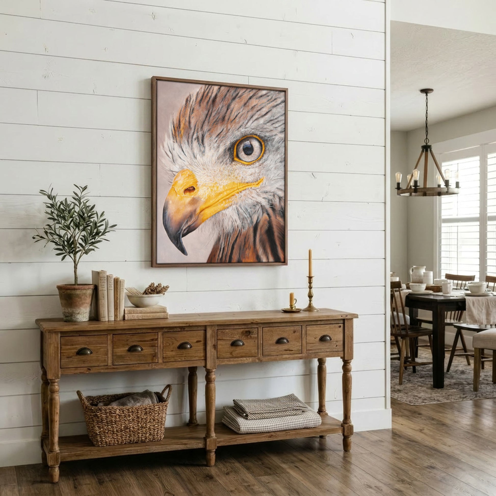 A framed vertical canvas print of an eagle's face hangs on a white shiplap wall above a rustic wooden console table in a bright, modern farmhouse dining room.