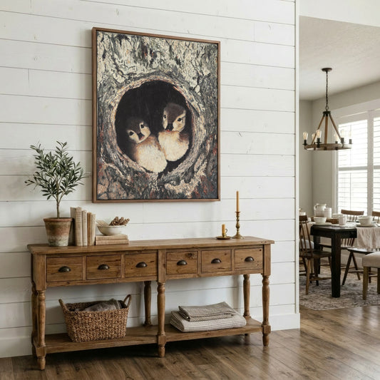 A large framed art print depicting two baby ducks in a tree hollow, styled on a white shiplap wall above a rustic wooden console table in a bright, modern farmhouse dining room.